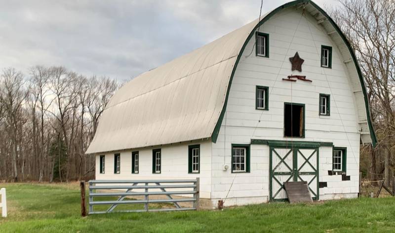 A white gambrel-roof barn with green trim beside a pasture gate in Howell, New Jersey
