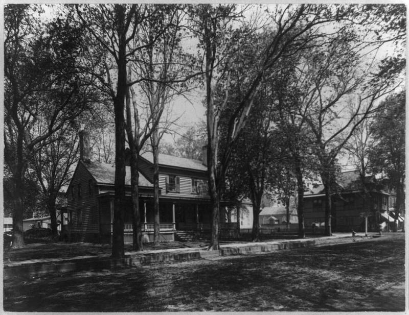 A 19th-century wooden house with a porch under tall trees in Freehold, 1896